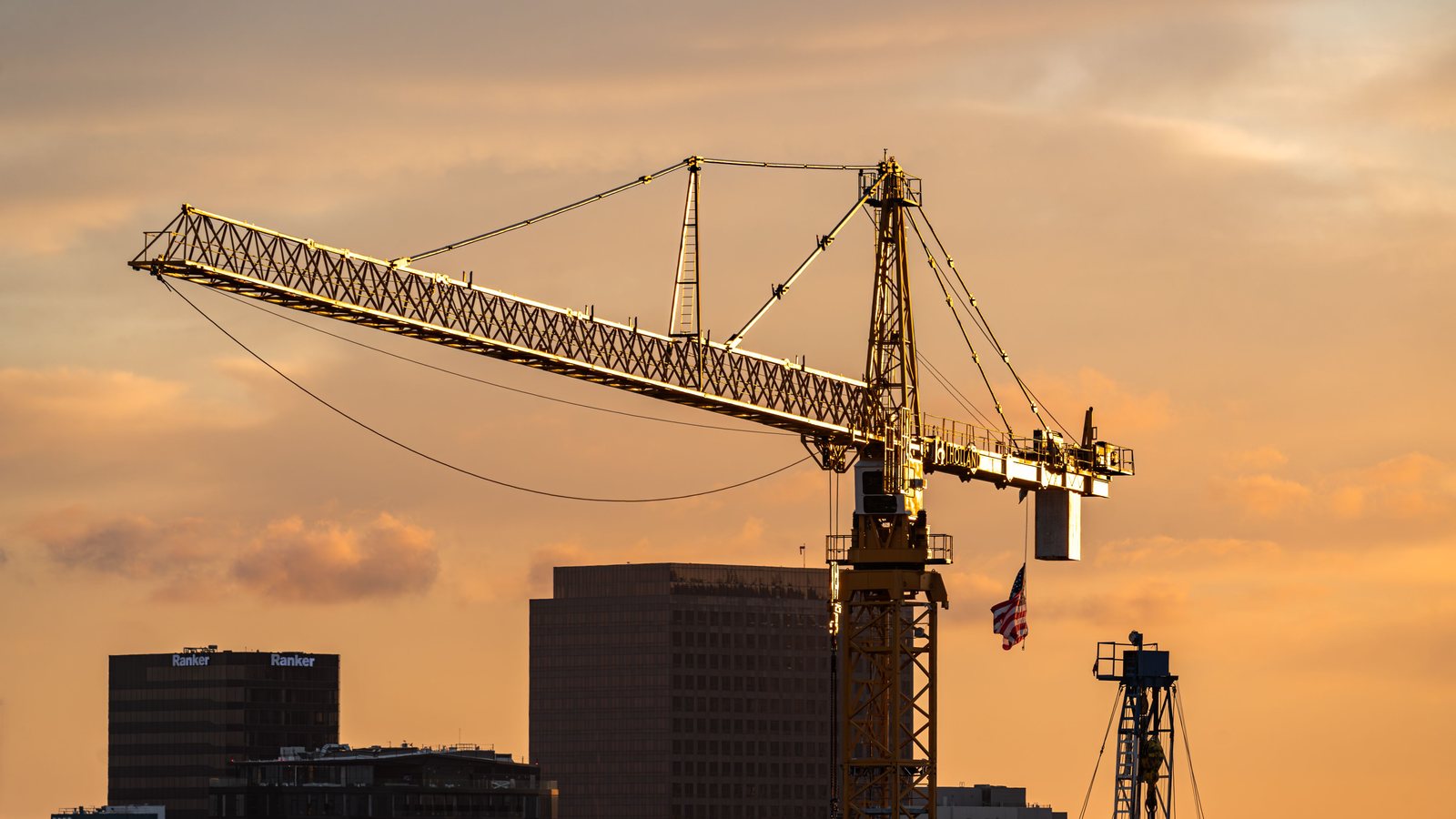 A tower crane silhouetted against a warm golden-hour sky above a residential building skyline.